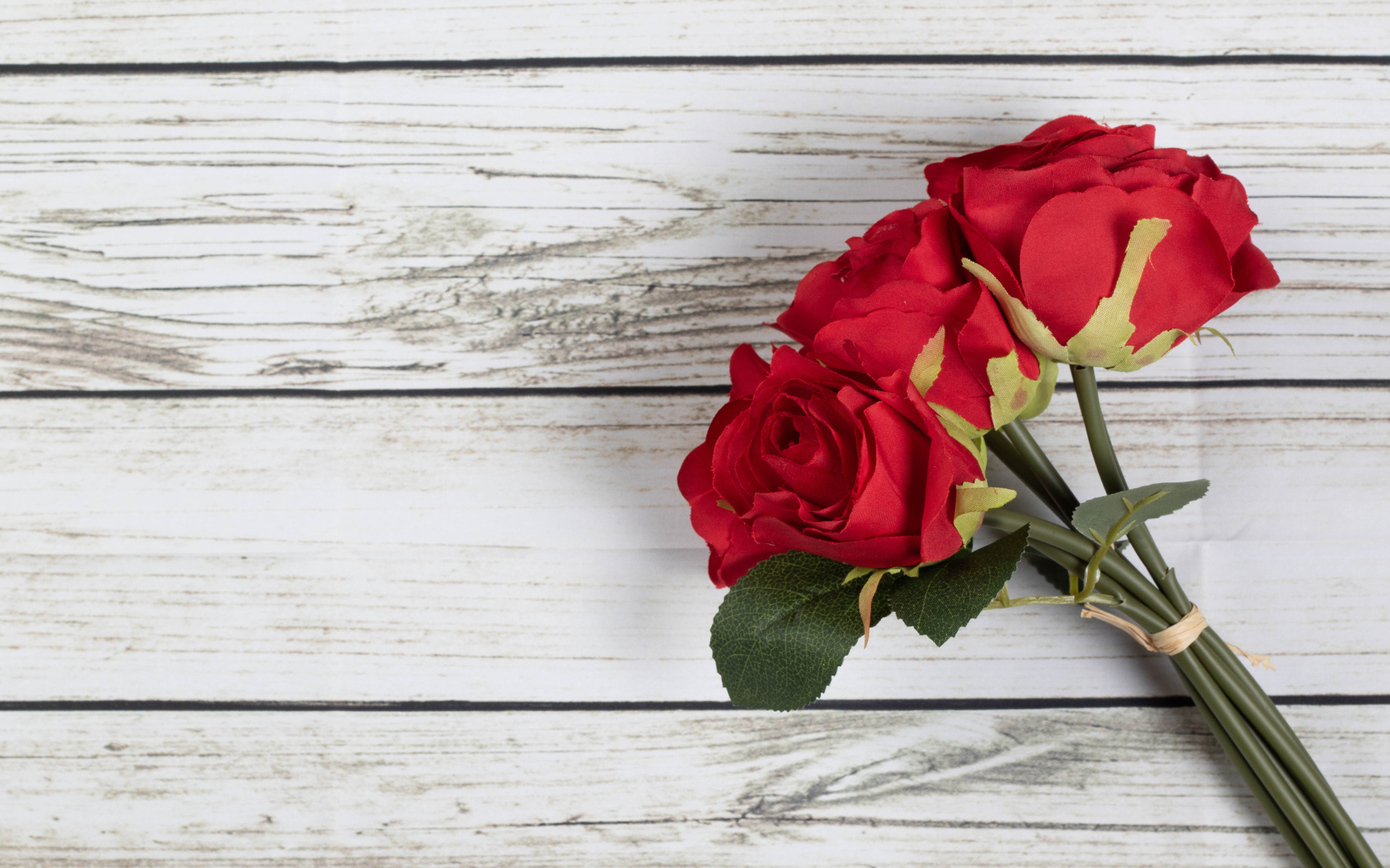 Три искусственные красные розы на деревянном фоне