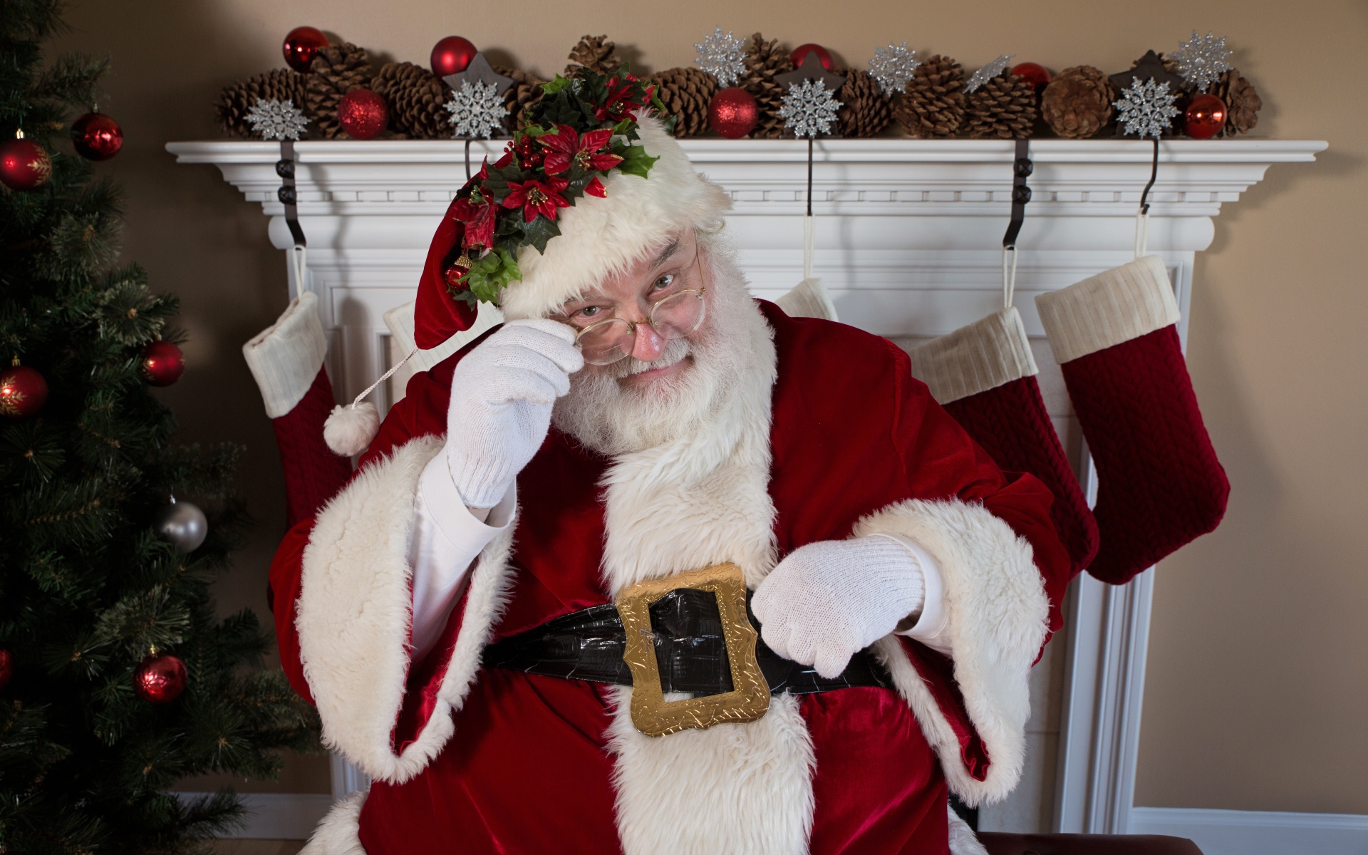 Санта Клаус в очках сидит у камина у новогодней елки