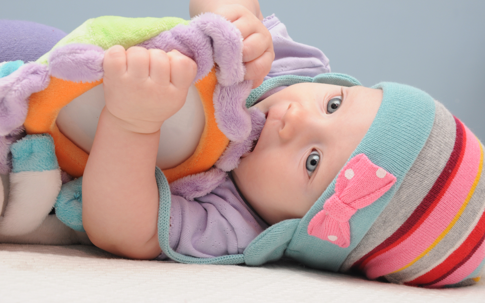 Младенец в шапке грызет мягкую игрушку