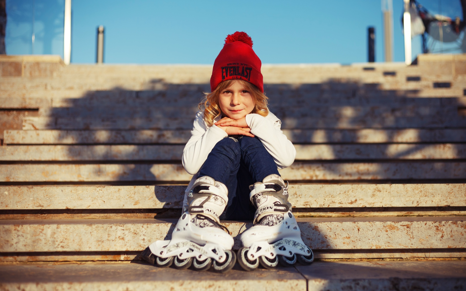 Маленькая девочка в роликах сидит на ступеньках 