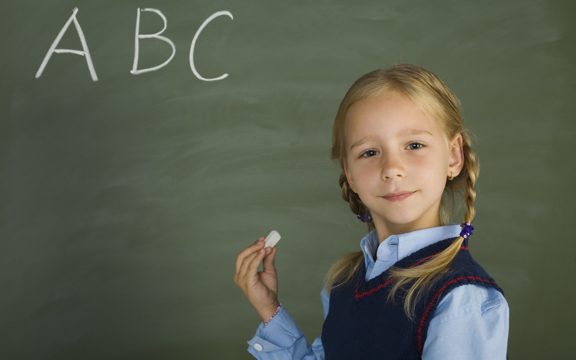 Маленькая школьница пишет буквы на доске 