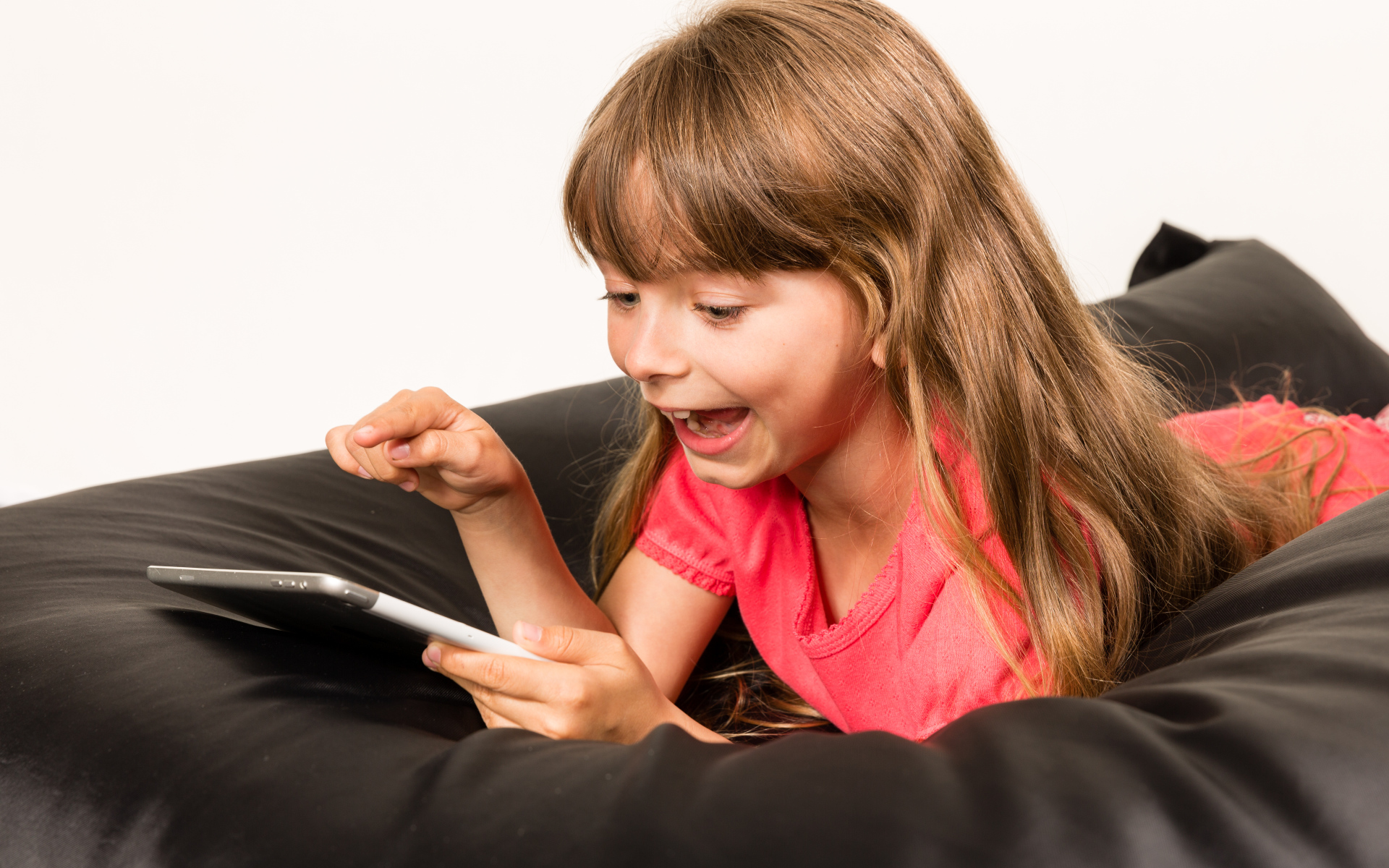 Маленькая улыбающаяся девочка лежит с планшетом