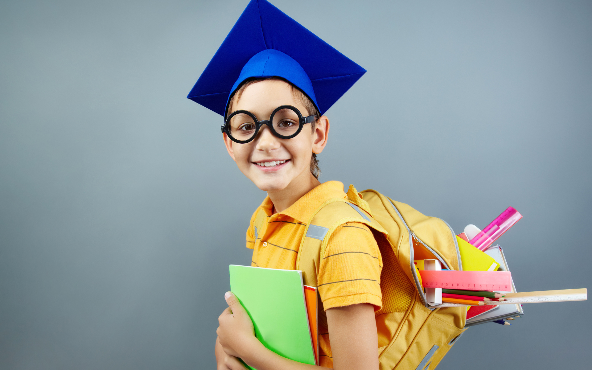 Умный школьник в очках со школьными принадлежностями на сером фоне