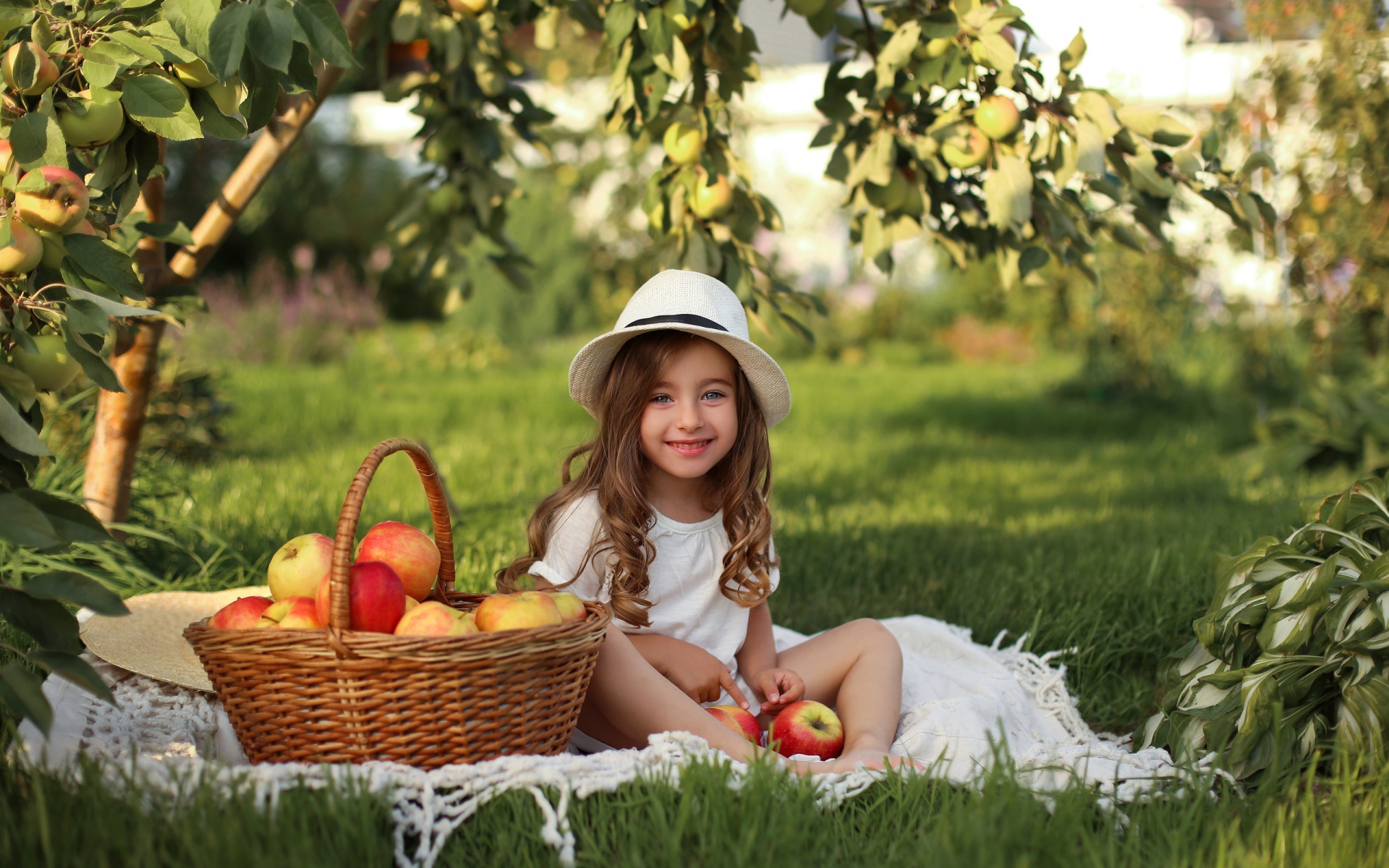 Улыбающаяся девочка сидит на зеленой траве с яблоками