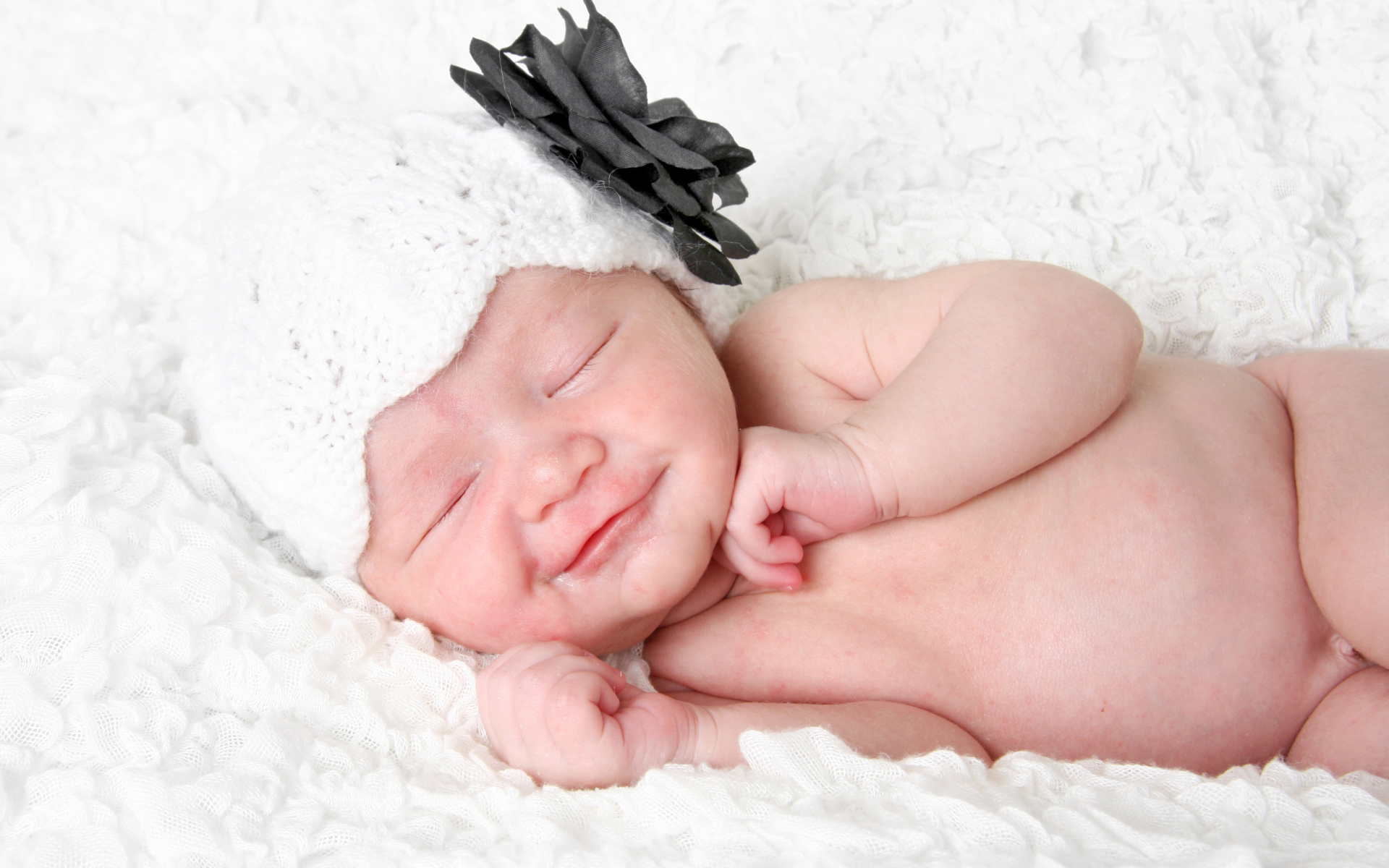 Улыбающийся спящий ребенок в белой вязаной шапке с цветком