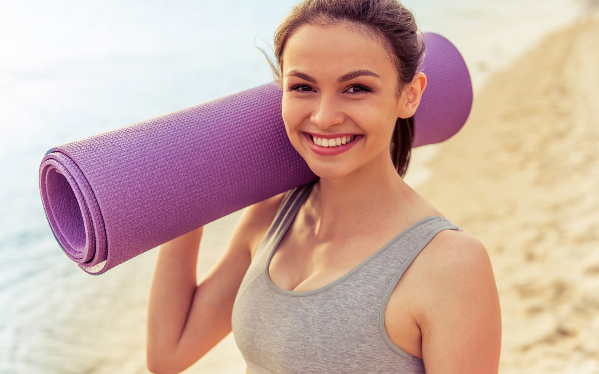 Спортивная девушка с ковриком для йоги на пляже