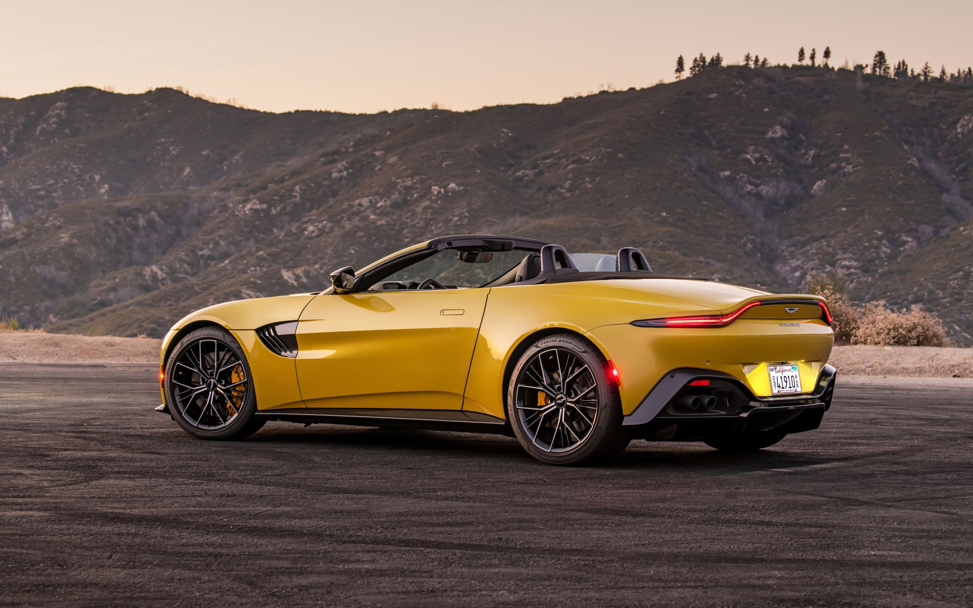 Желтый автомобиль  Aston Martin Vantage Roadster, 2021 года на фоне гор 