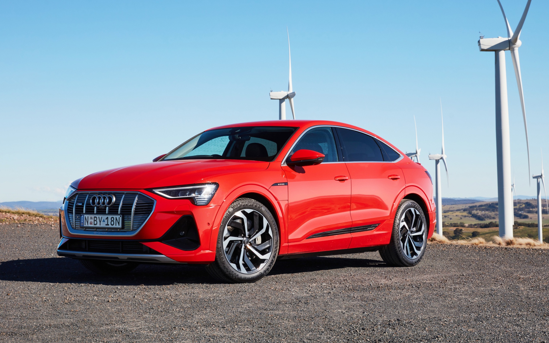 Красный автомобиль Audi E-Tron 50 Quattro Sportback S Line 2020 на фоне ветряных турбин