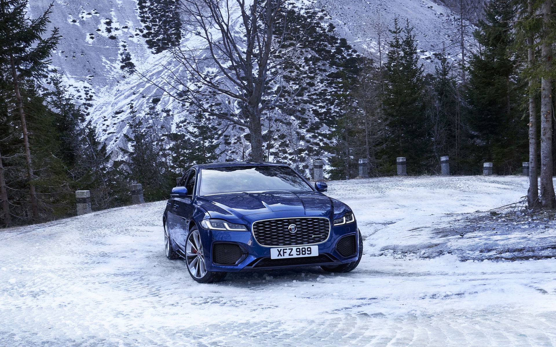 Синий автомобиль Jaguar XF зимой на фоне горы 