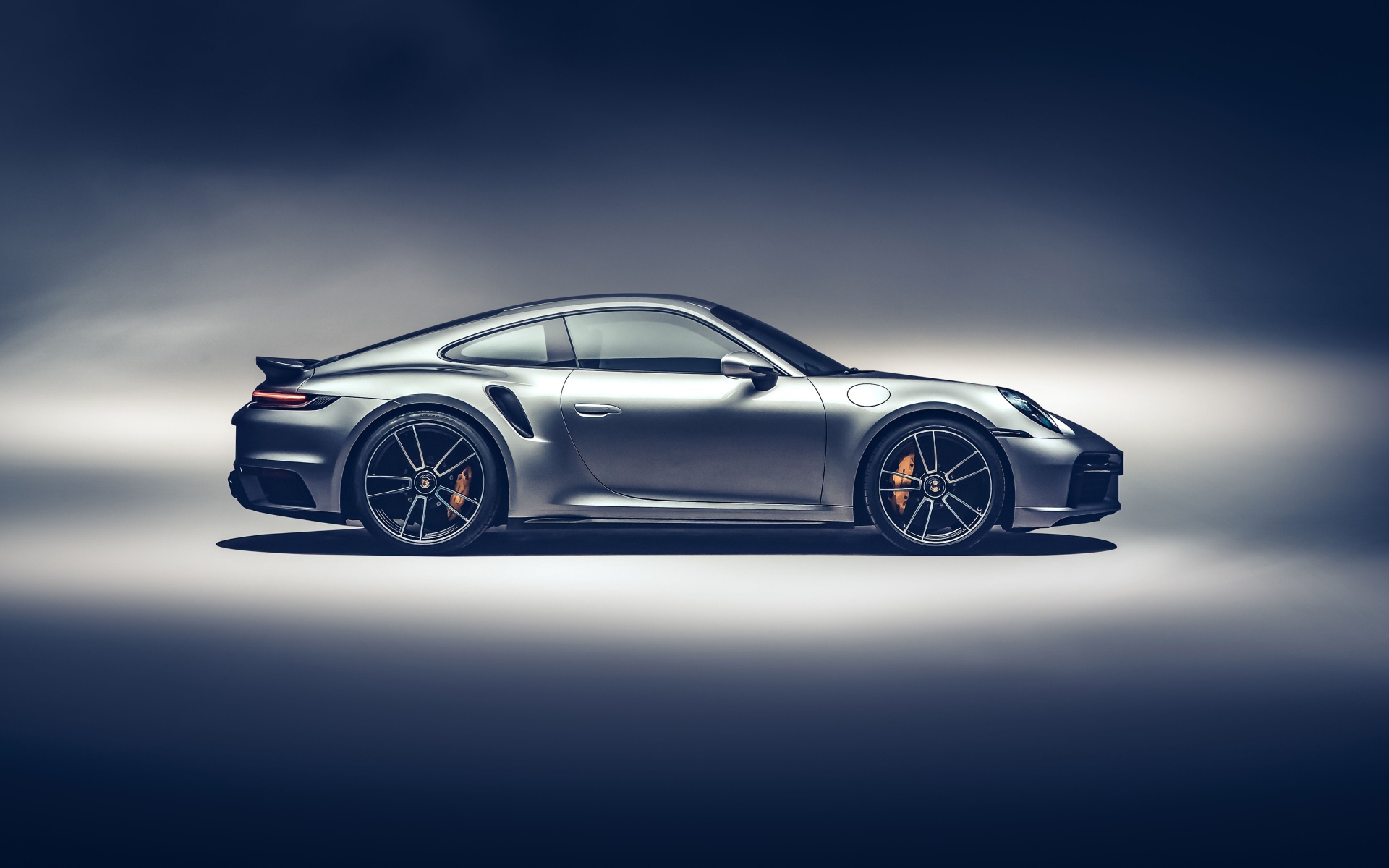 Серебристый автомобиль Porsche 911 Turbo S 2020 года вид сбоку на сером фоне