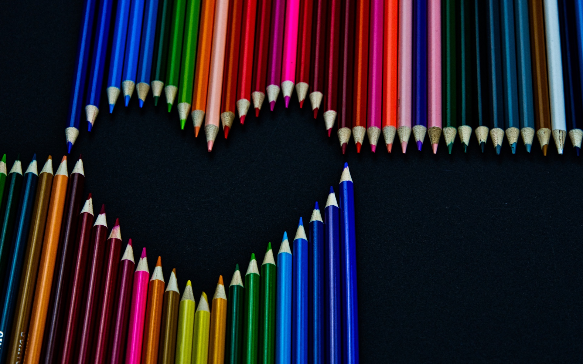 Сердце из разноцветных карандашей на черном фоне