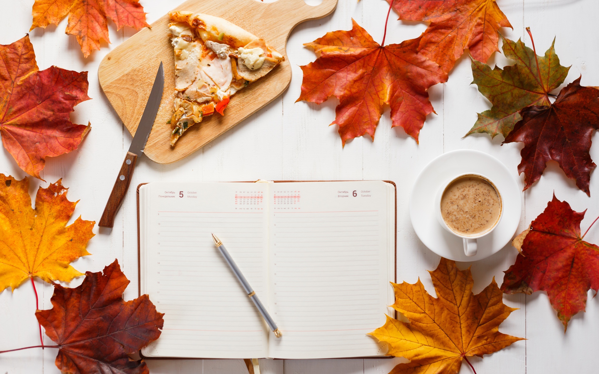 Ежедневник на столе с желтыми листьями, кофе и пиццей 