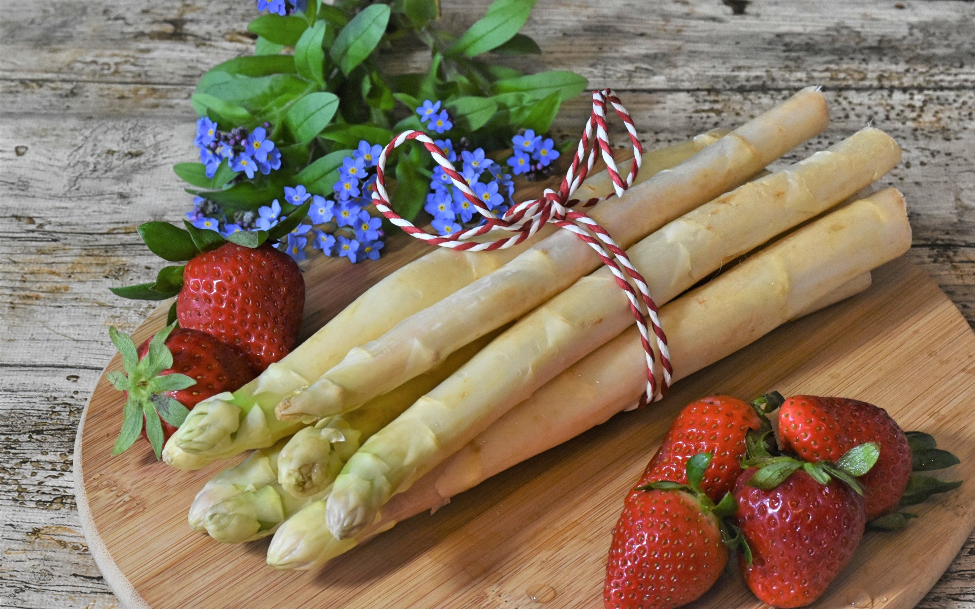 Свежая спаржа на столе с клубникой и цветами незабудками