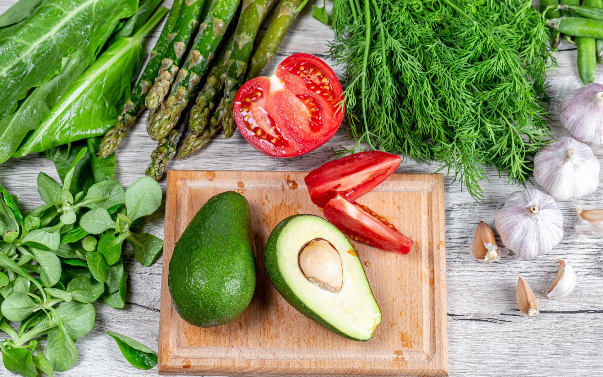 Свежая зелень на столе с авокадо, помидором и чесноком