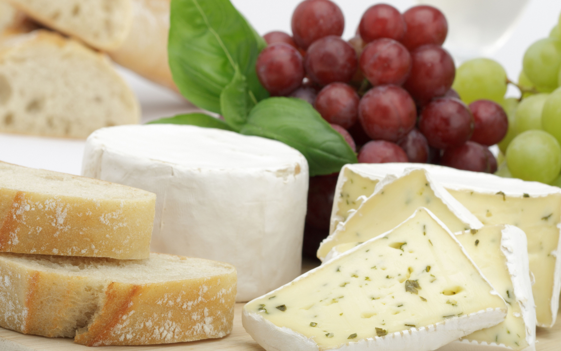 Твердый сыр на столе с батоном и виноградом