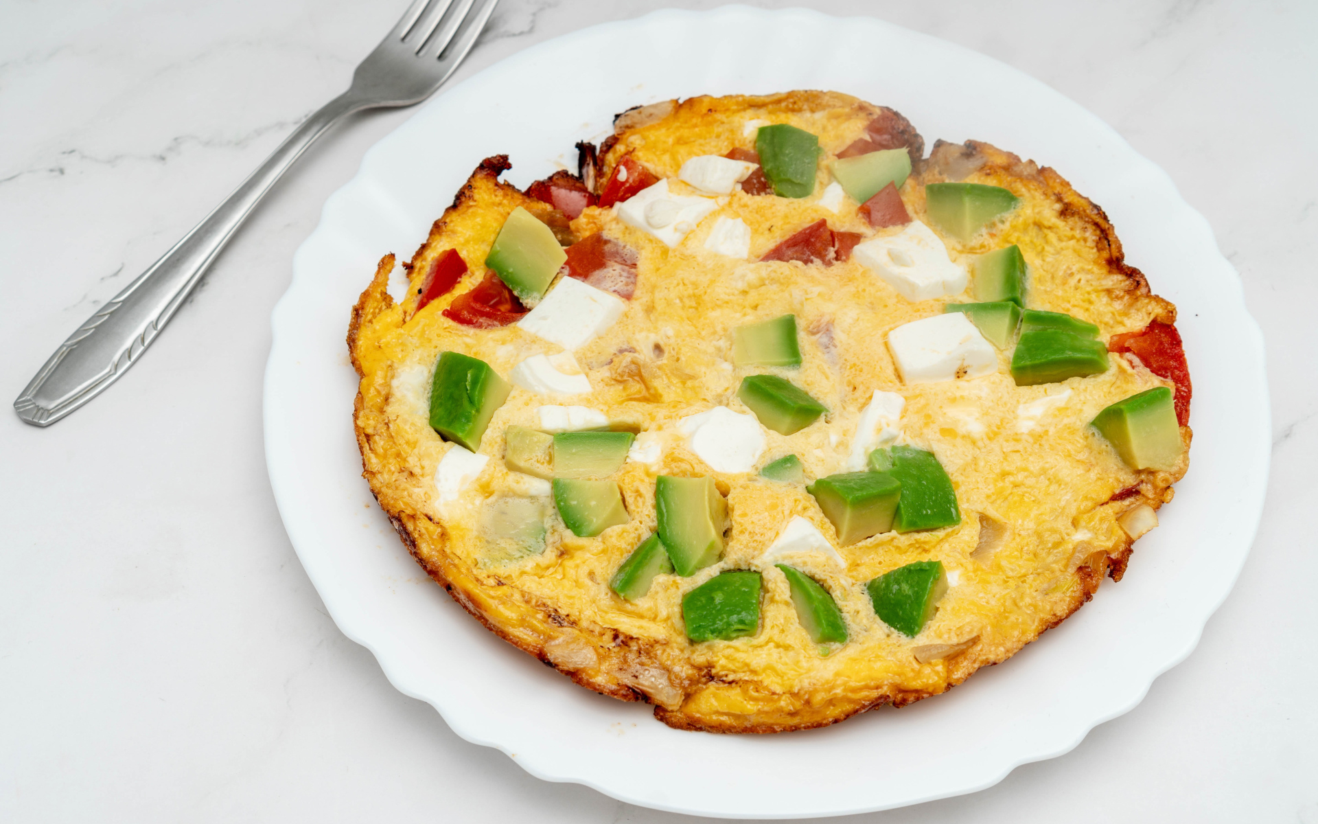 Омлет с авокадо и кусочками помидора на белой тарелке 