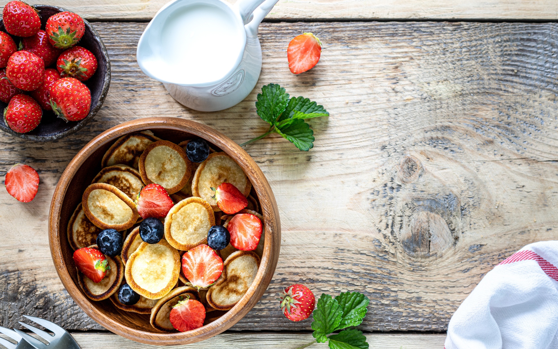 Маленькие оладьи в миске с клубникой и черникой на столе с молоком 