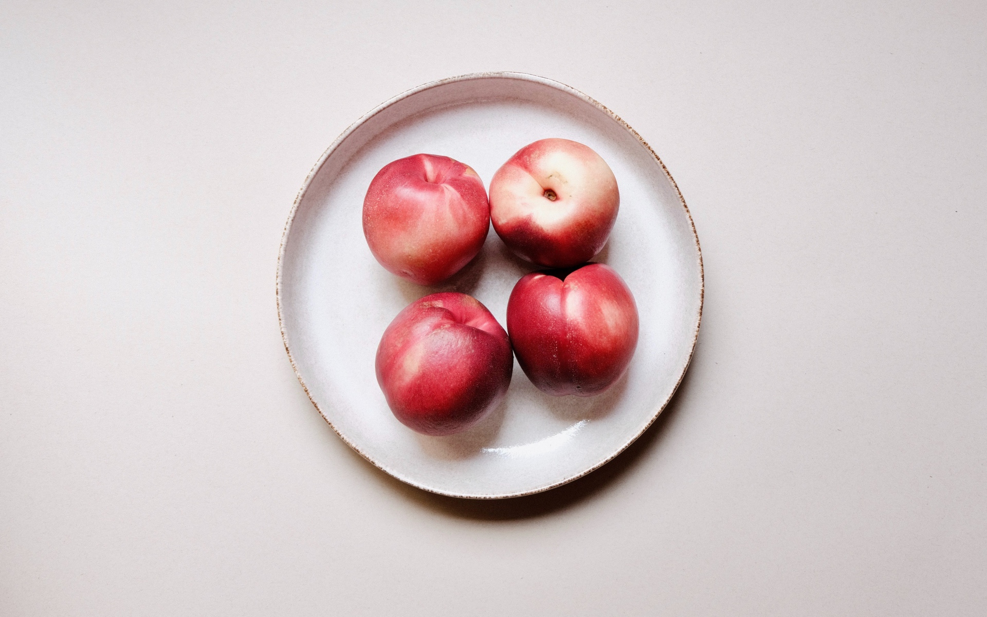 Четыре красных спелых нектарина на тарелке 