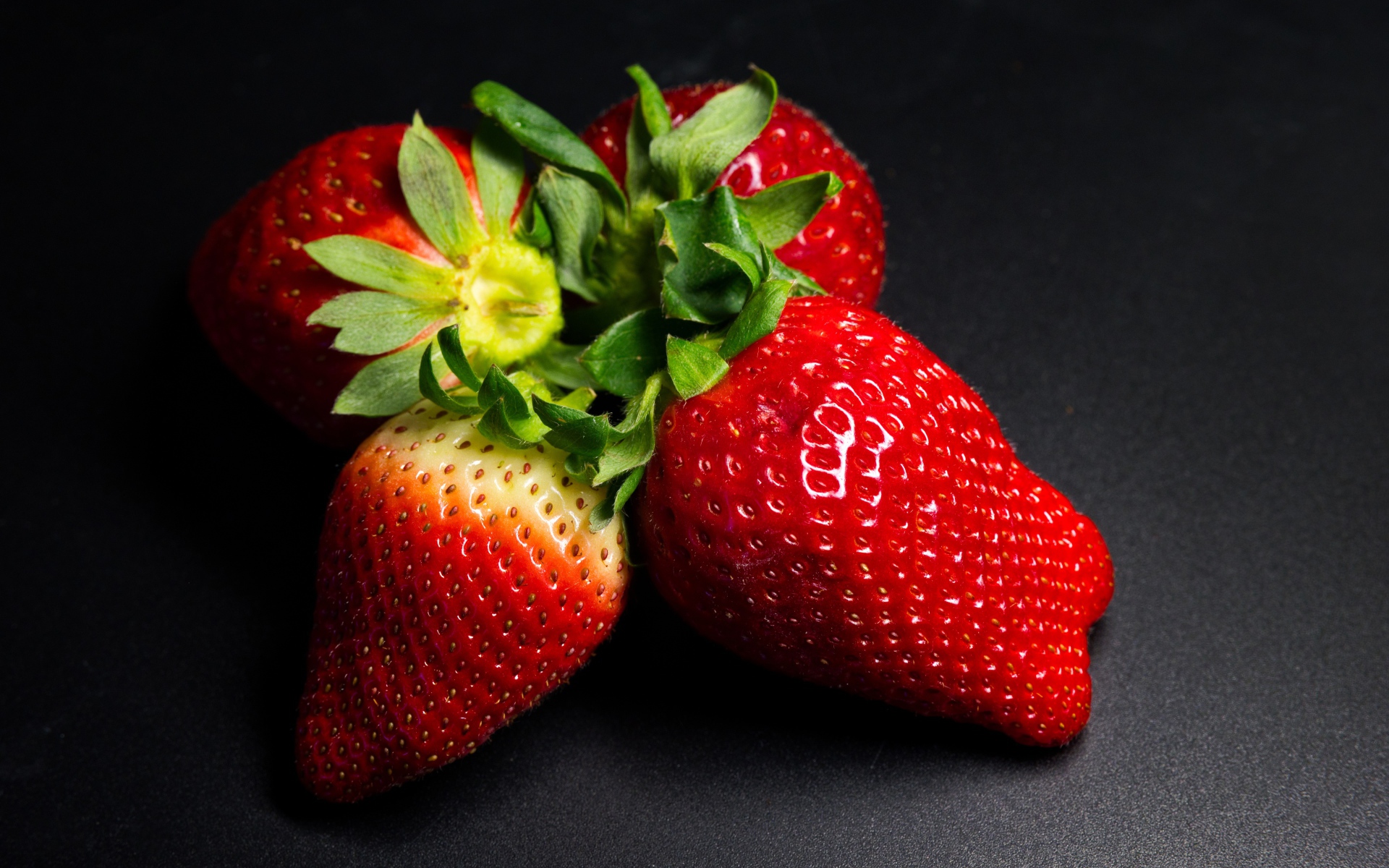 Четыре спелых красных ягоды клубники на черном столе 
