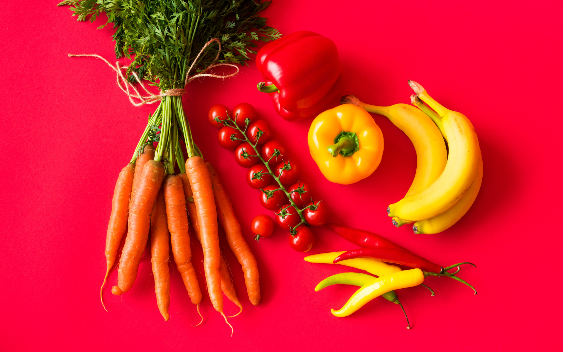 Свежие морковь, помидоры, перец и бананы на красном фоне