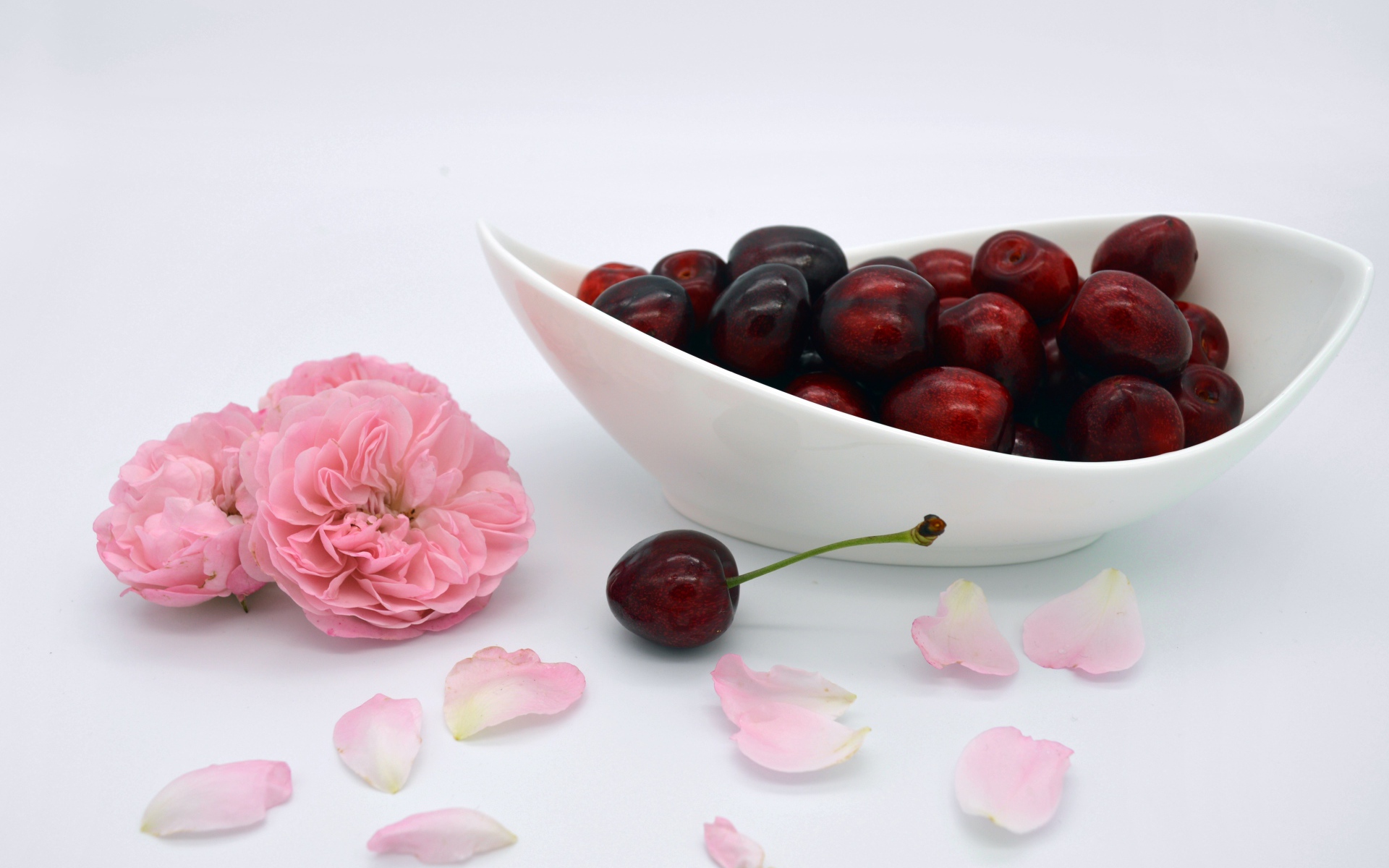 Белая тарелка с красными ягодами черешни на столе с цветами