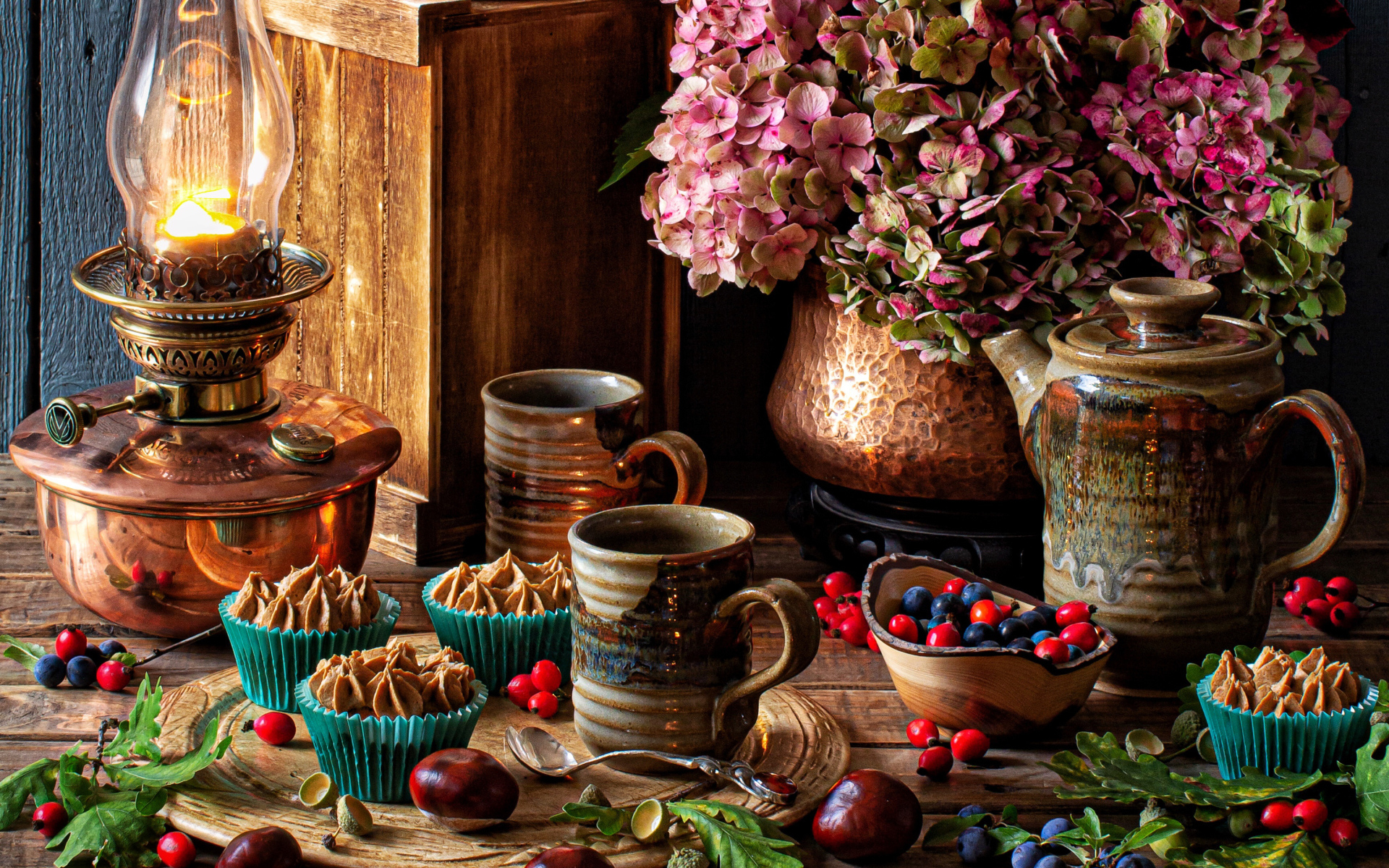 Кексы с кремом на столе с ягодами, цветами и лампой 