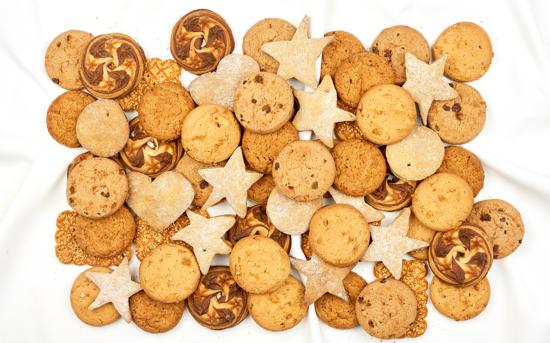 Много песочного печенья разной формы на белом фоне