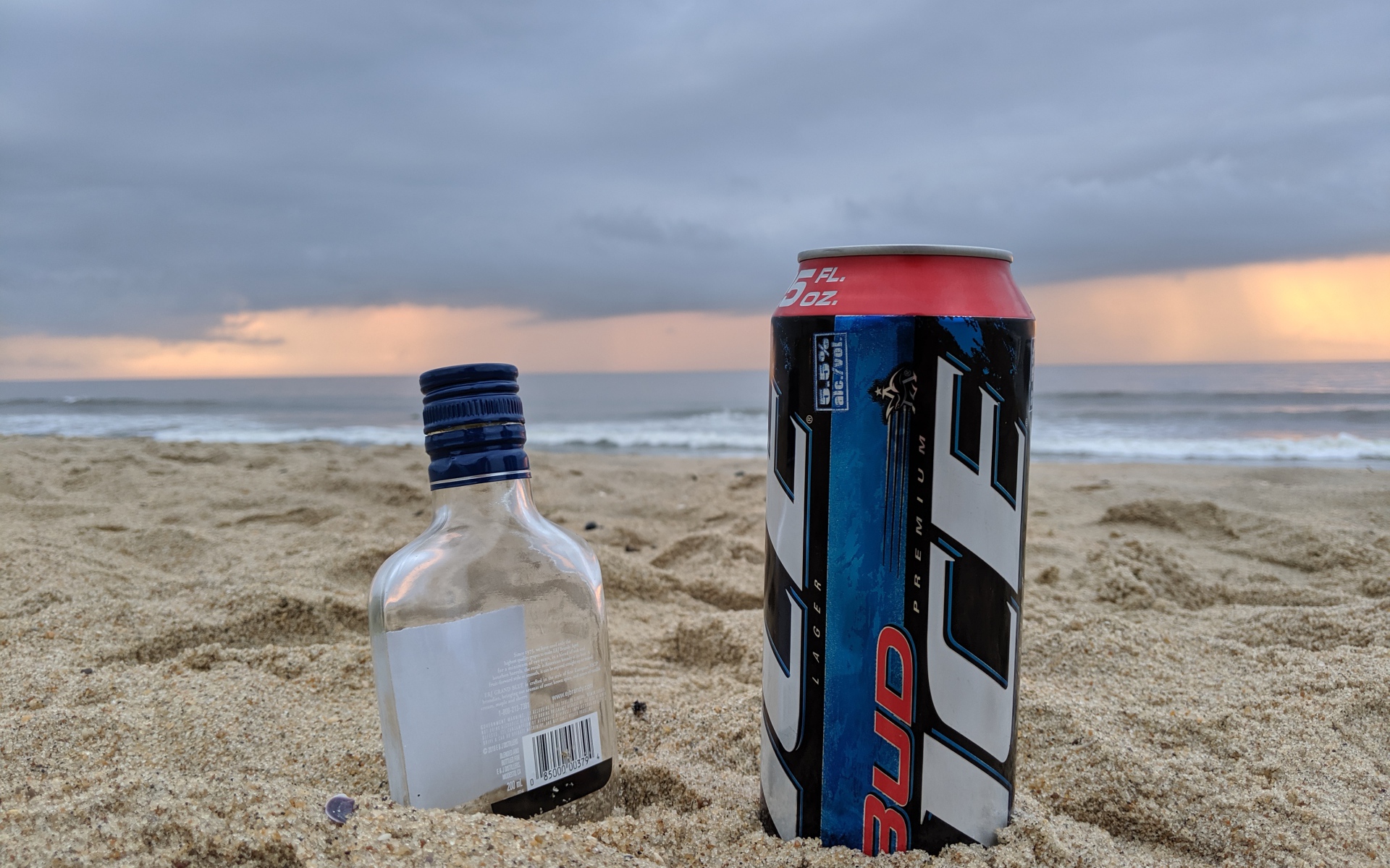 Бутылка пива и бутылка водки на песке у моря