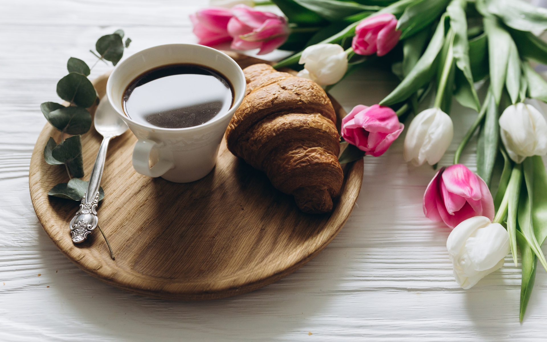 Чашка кофе и круассан на столе с букетом тюльпанов