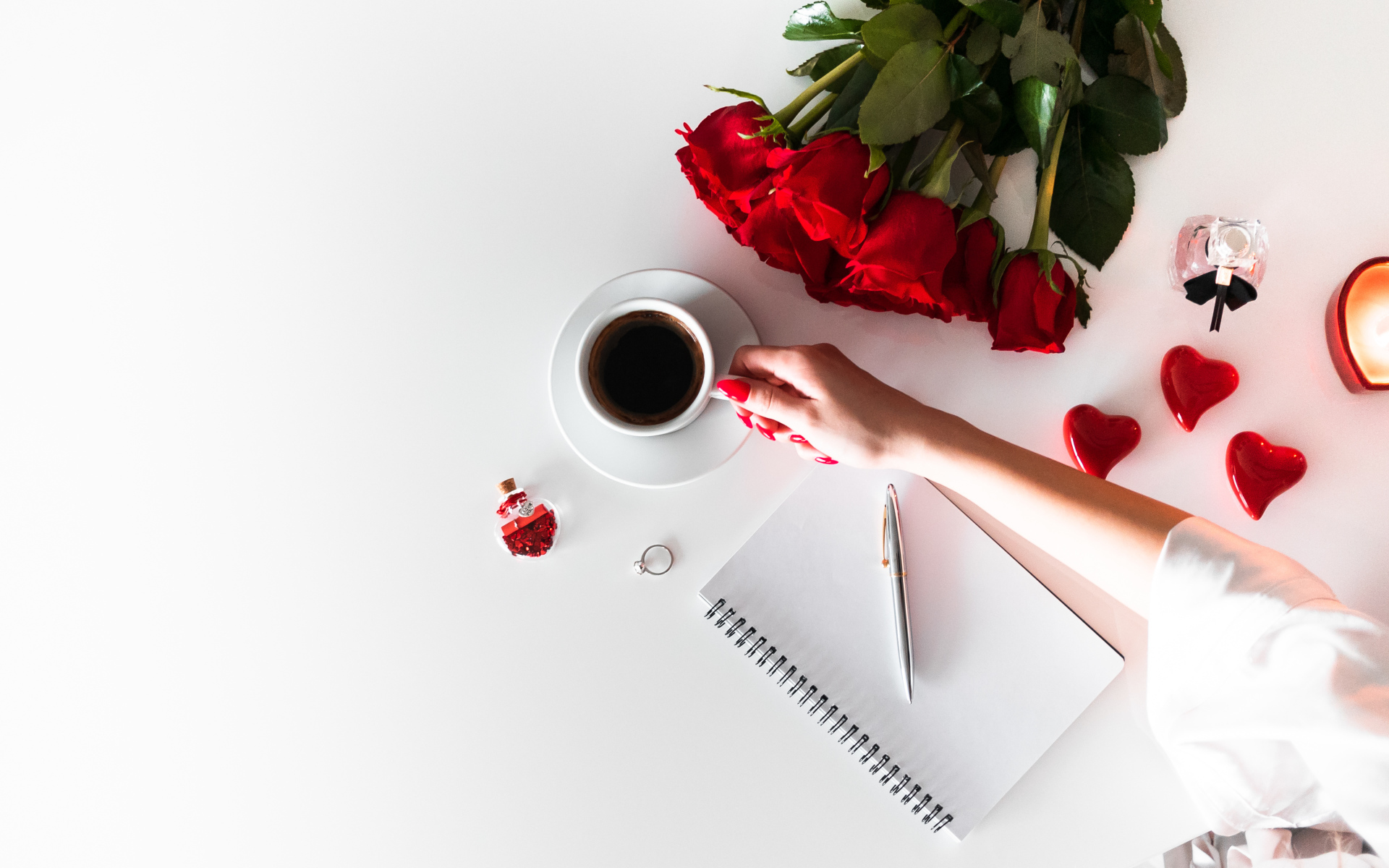 Девушка держит в руках чашку кофе на столе с блокнотом и букетом роз 