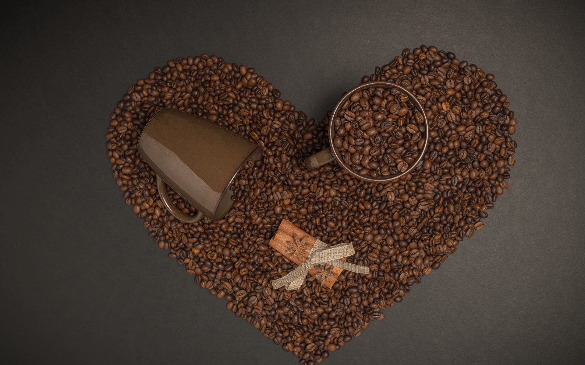 Heart made of coffee beans on a gray background with mugs