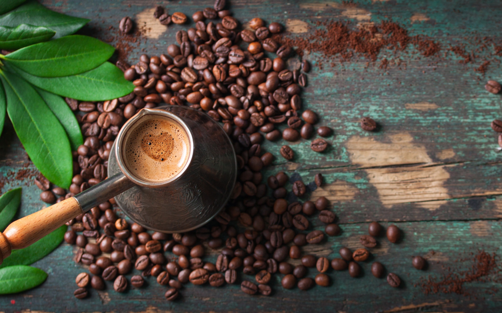 Турка с кофе на столе с зернами и зелеными листьями
