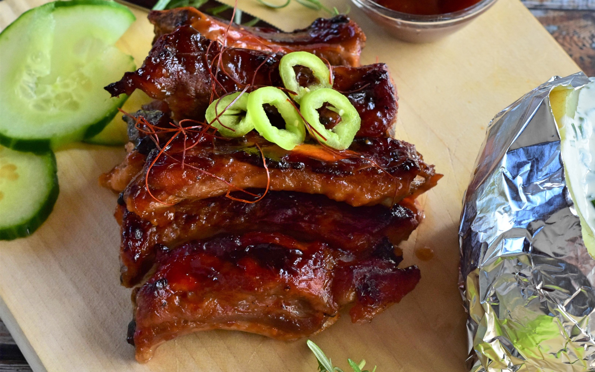 Аппетитные жареные ребрышки на столе с огурцами  и соусом 