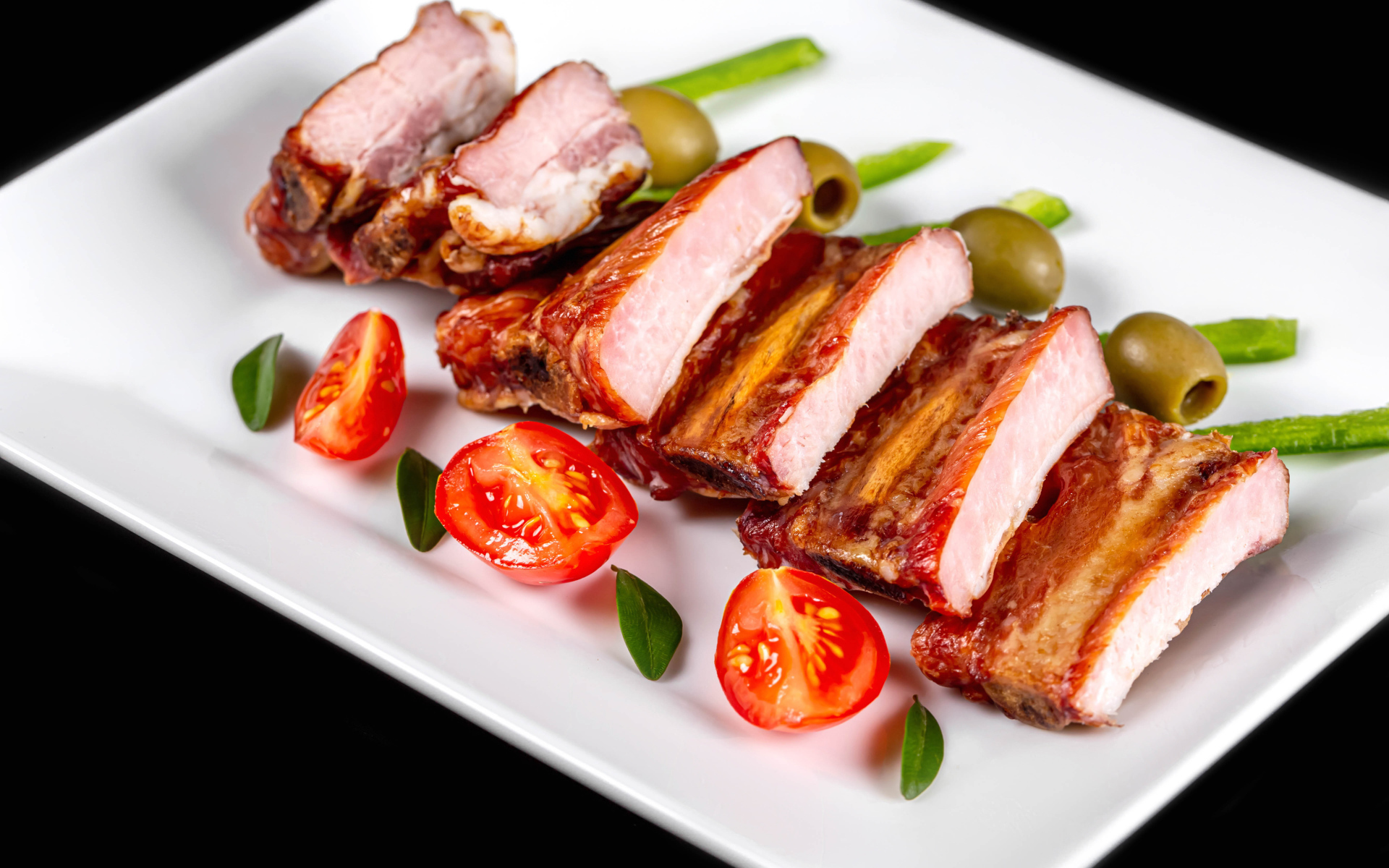 Запеченные ребрышки на белой тарелке с помидорами и оливками