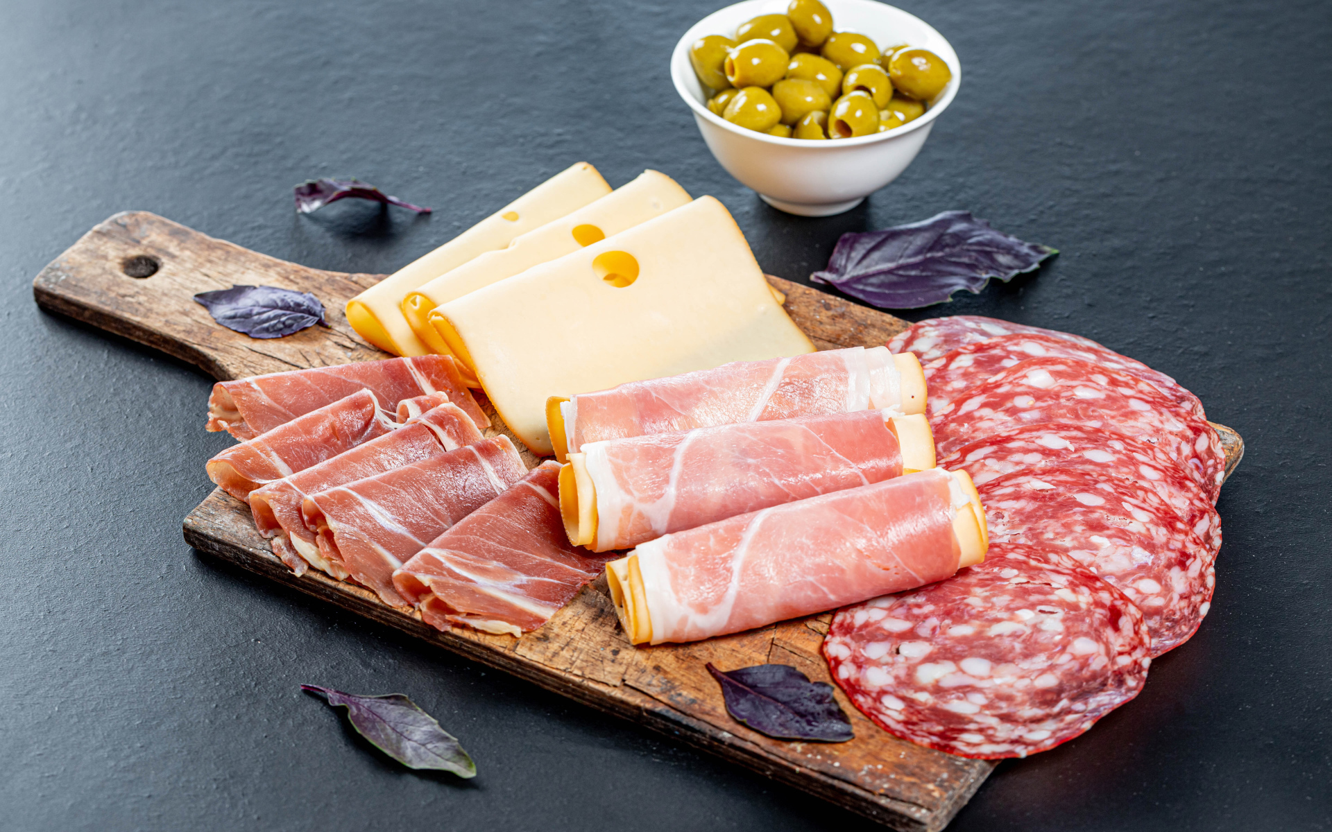 Сыр, бекон и колбаса на разделочной доске на столе с оливками