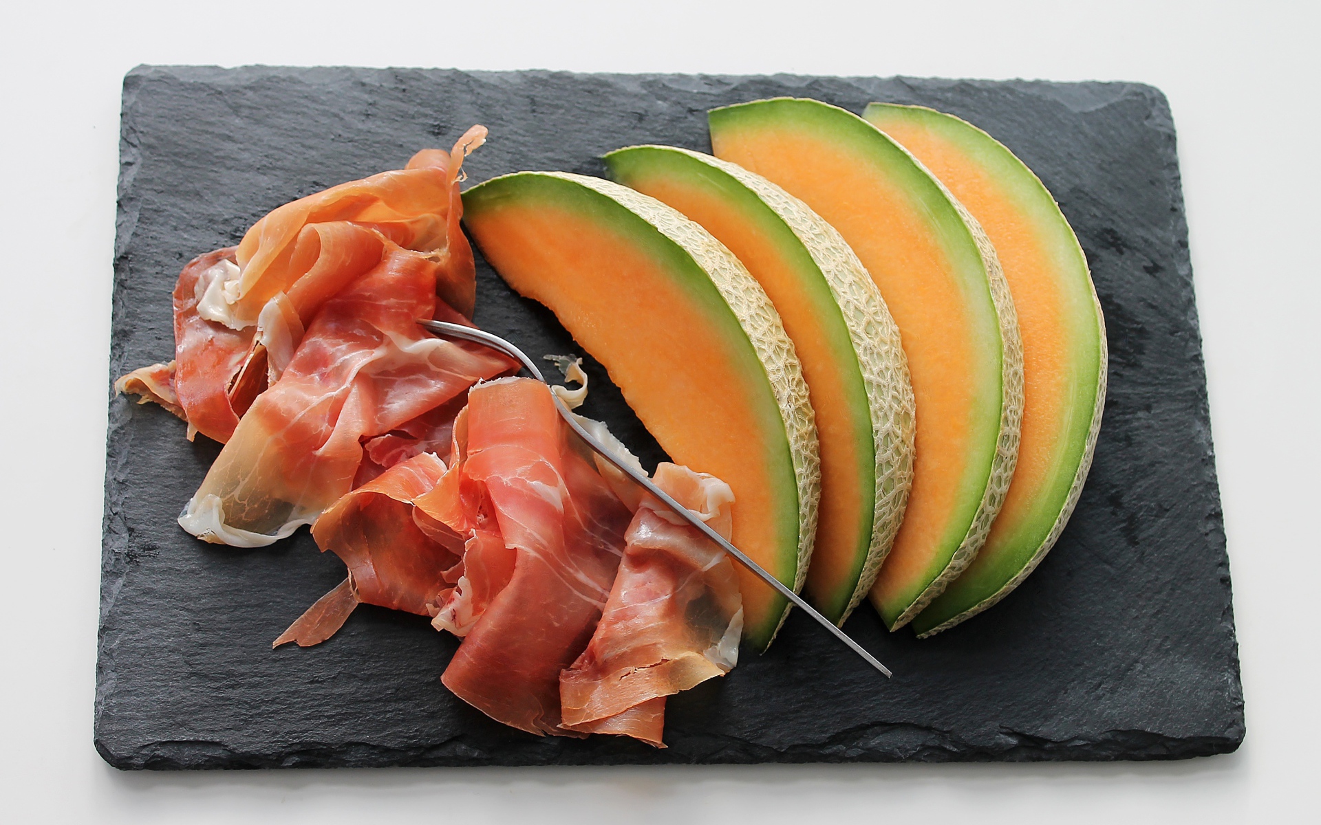 Кусочки дыни на доске с прошутто