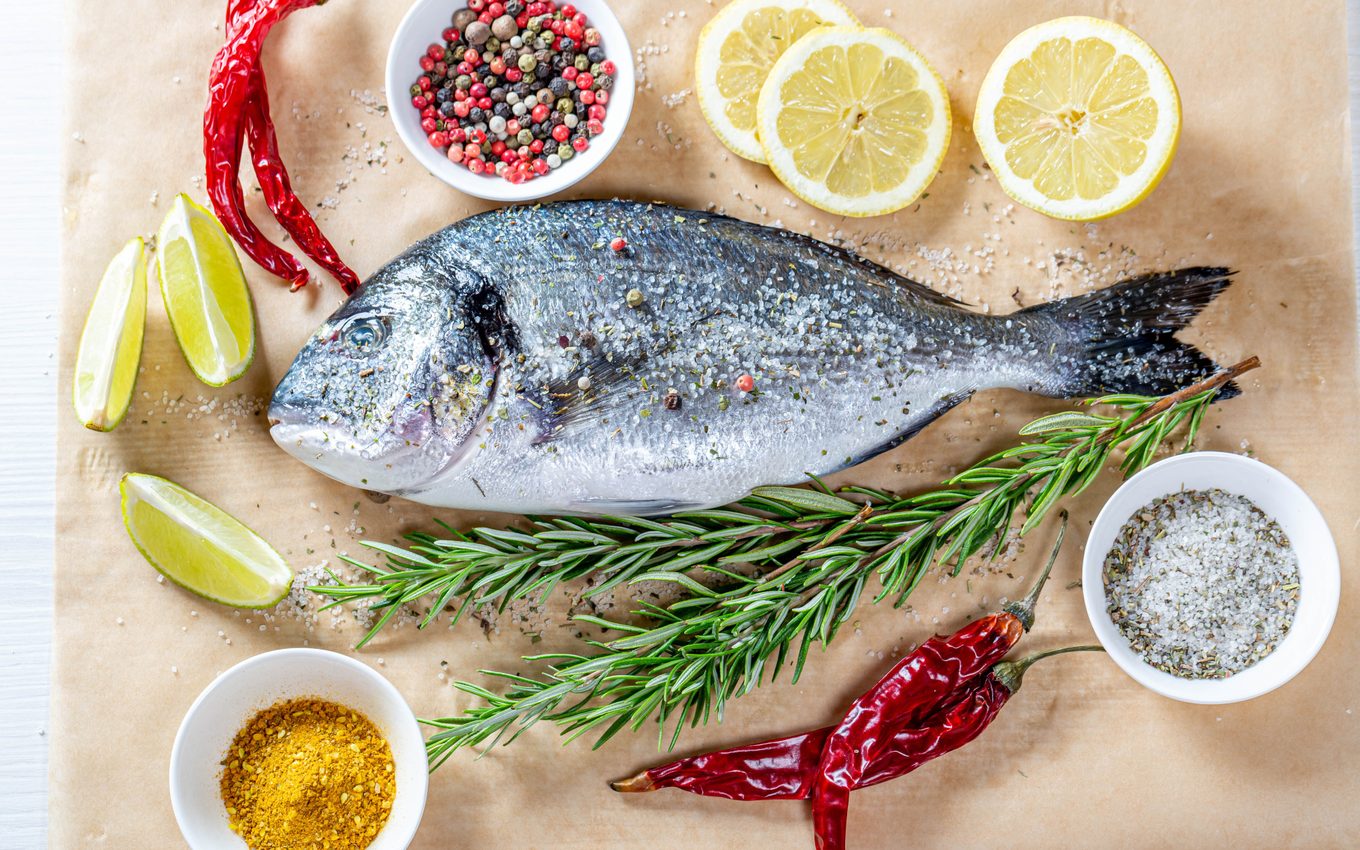 Свежая рыба на столе со специями, лимоном, розмарином и красным перцем