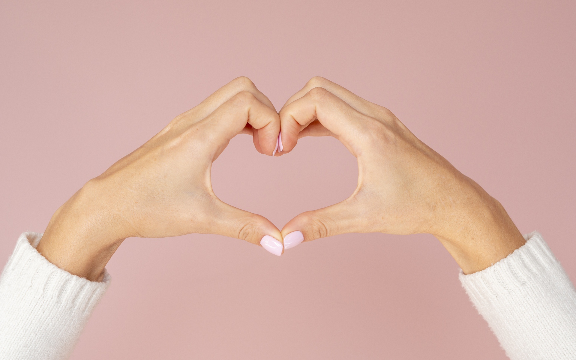 Девушка делает сердце руками на розовом фоне 