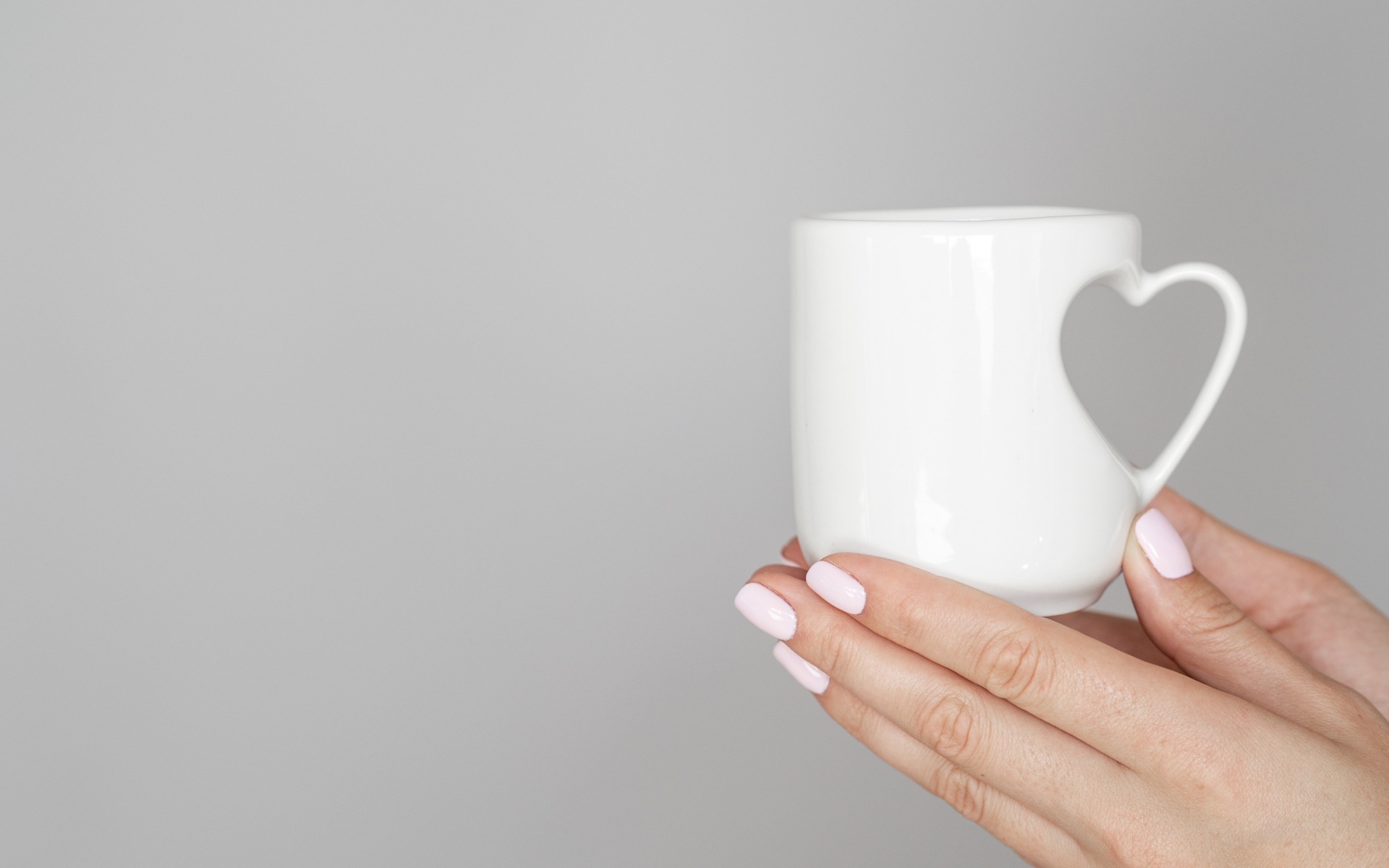 White mug in the hands of a girl on a gray background