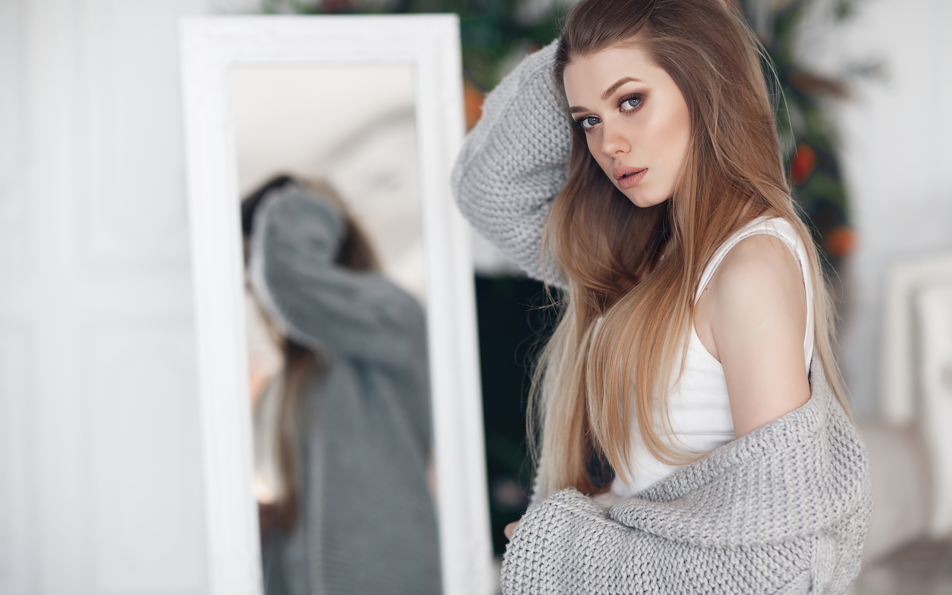 Молодая девушка в серой кофте стоит у зеркала 