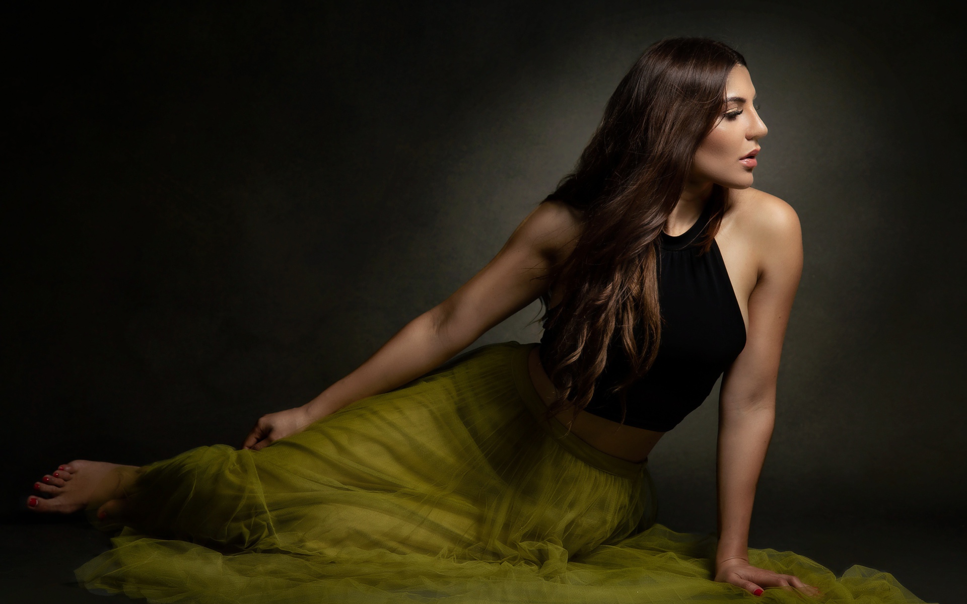 Молодая девушка в длинной юбке сидит на полу