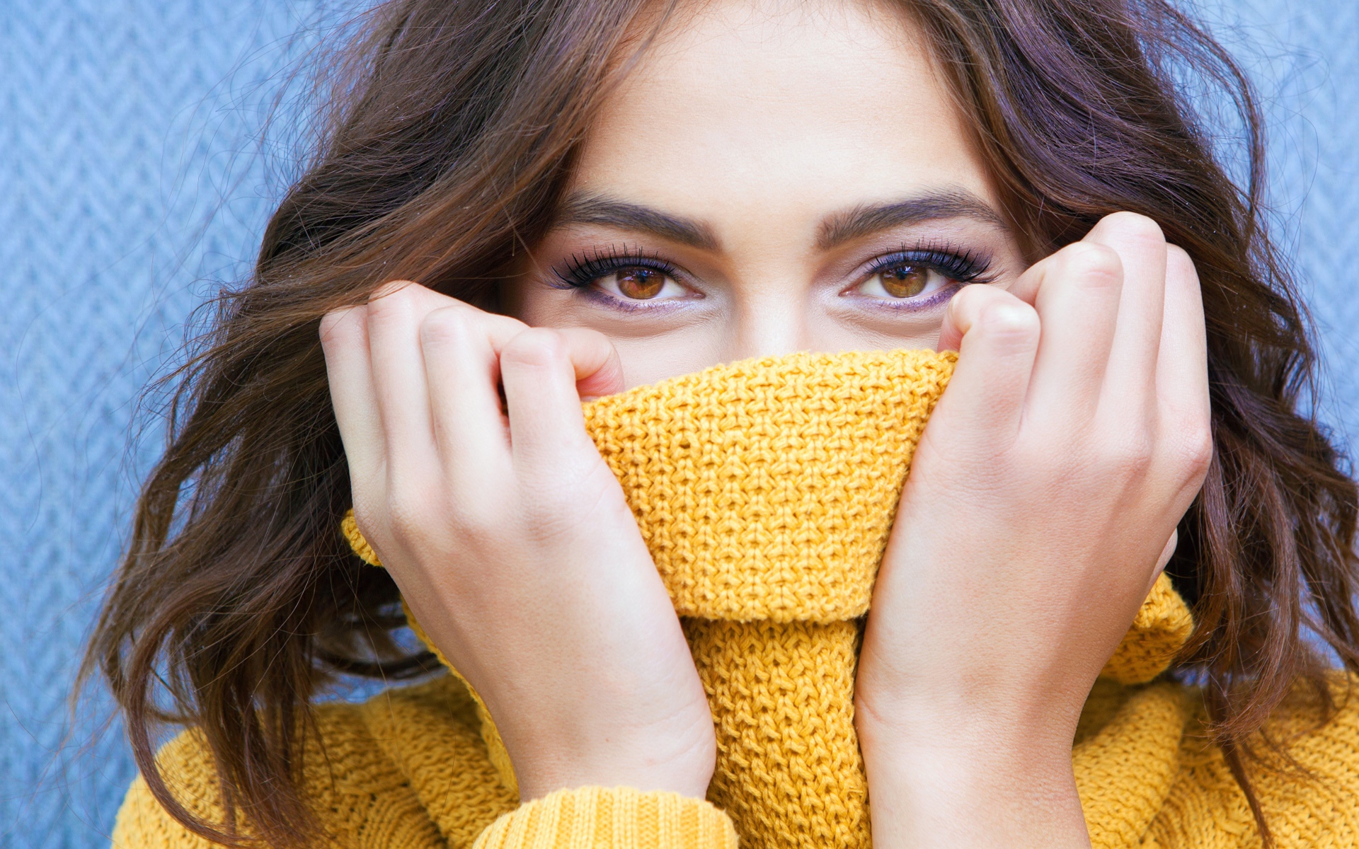 Красивая кареглазая девушка закрывает лицо свитером