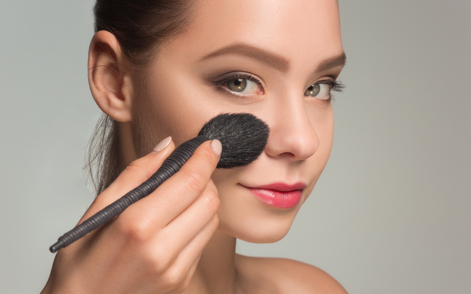 Красивой девушке наносят макияж на лицо кистью 