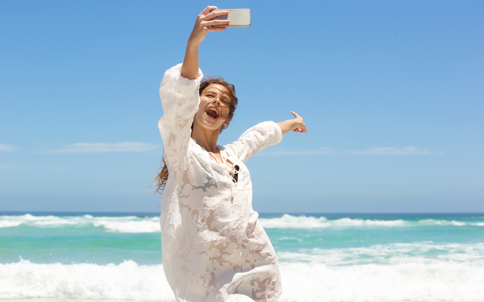 Красивая девушка в белом платье делает селфи на море 