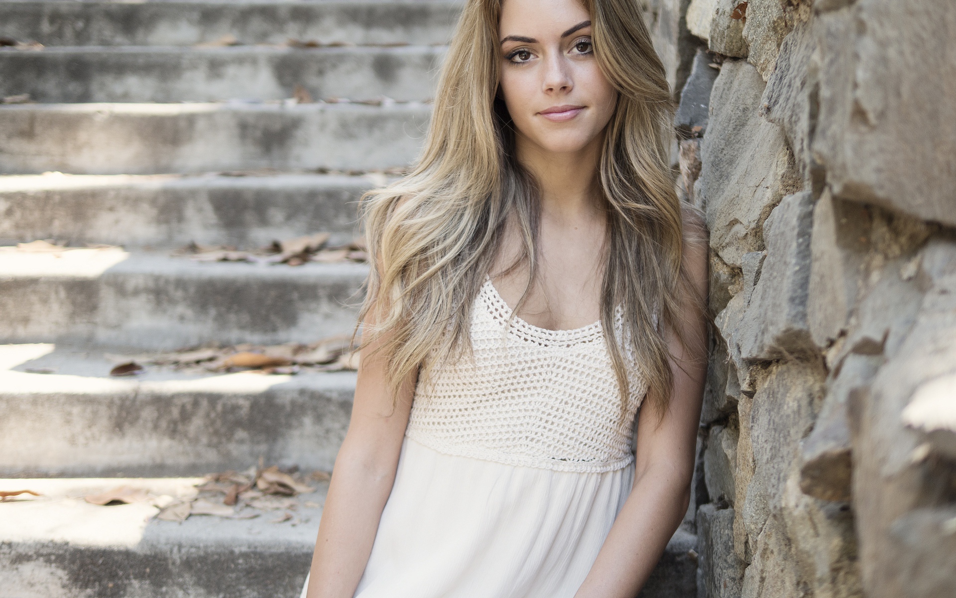Красивая девушка в белом платье у каменной стены 