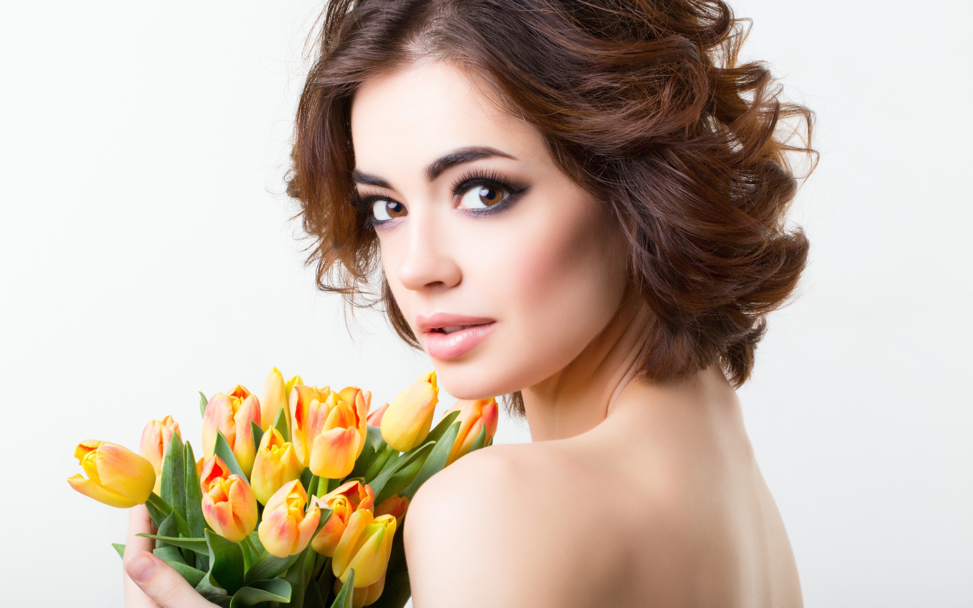 Красивая девушка с прической в букетом тюльпанов в руках на белом фоне