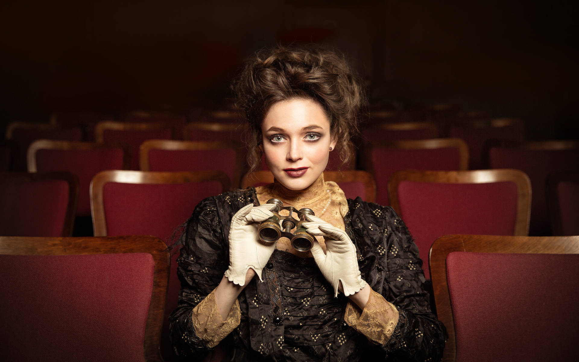 Красивая девушка с биноклем сидит в театре