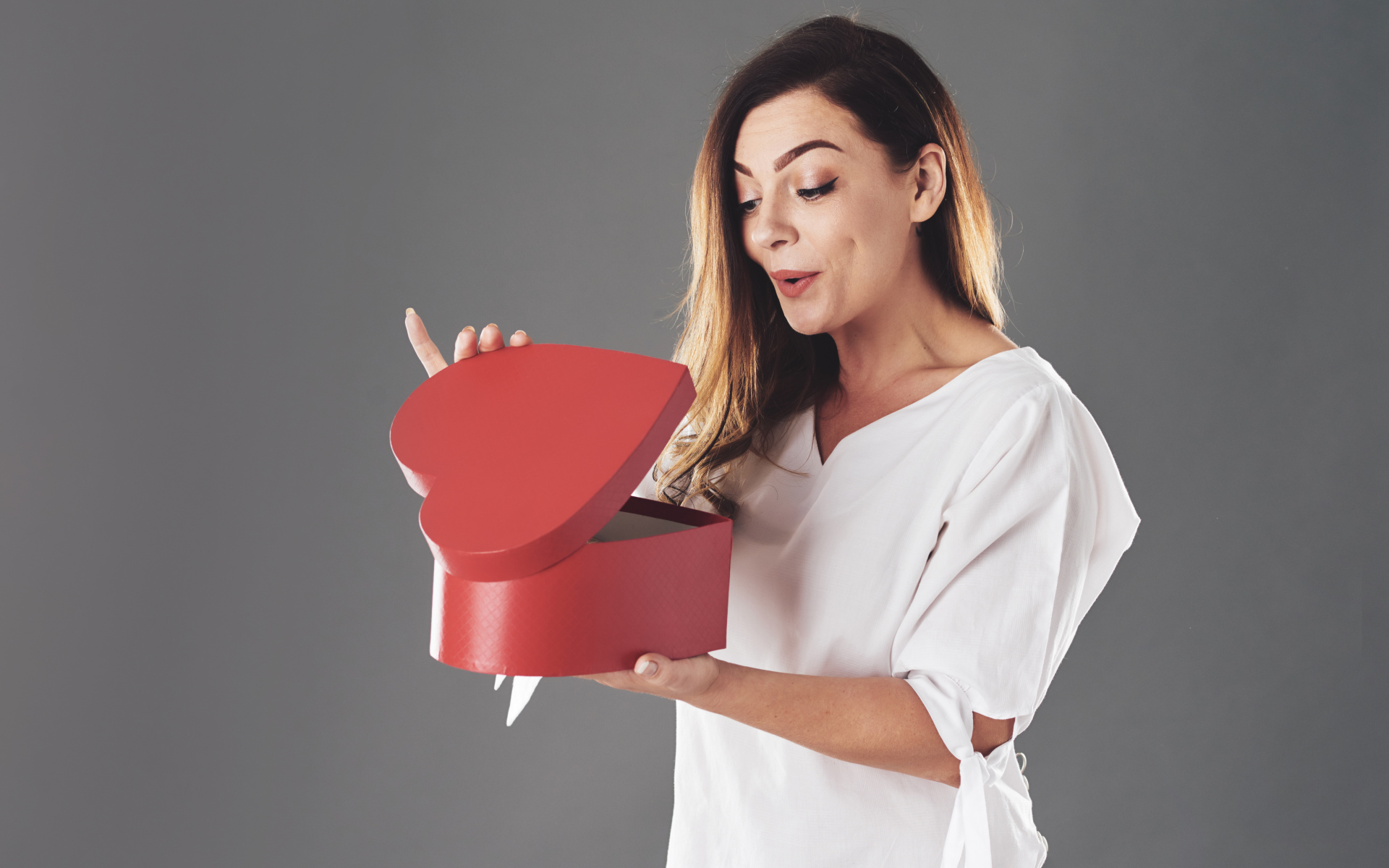 Любопытная девушка смотрит в красную коробку в форме сердца