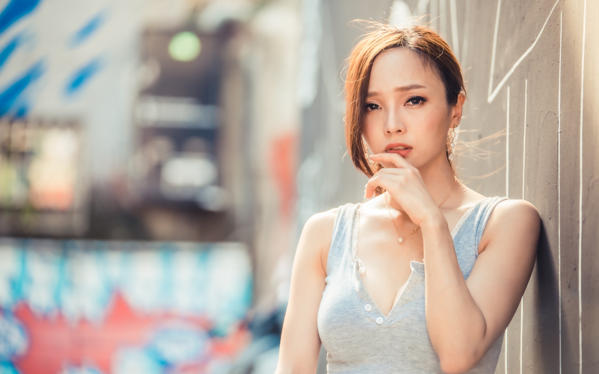 Милая девушка азиатка  с рукой у лица стоит у стены 