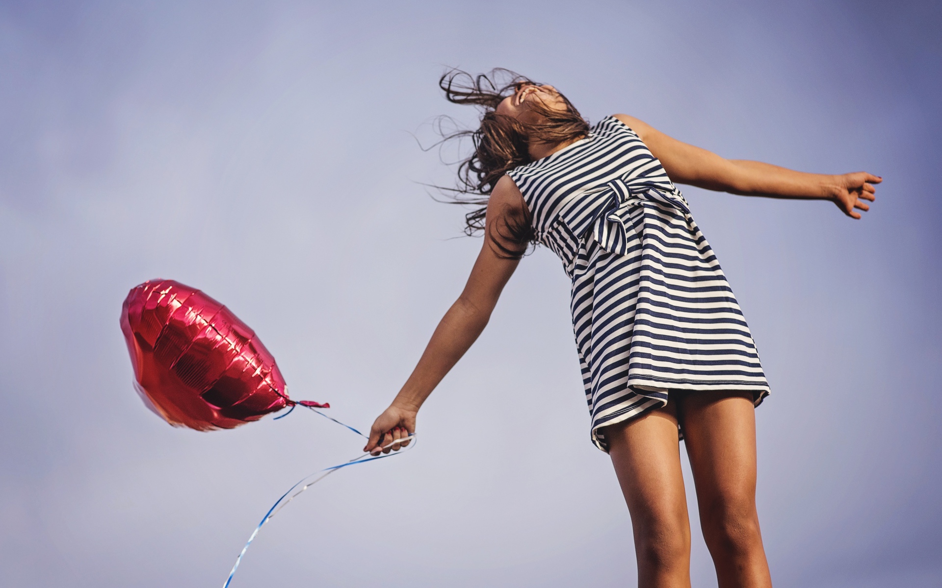 Девушка в полосатом платье прыгает с шариком 